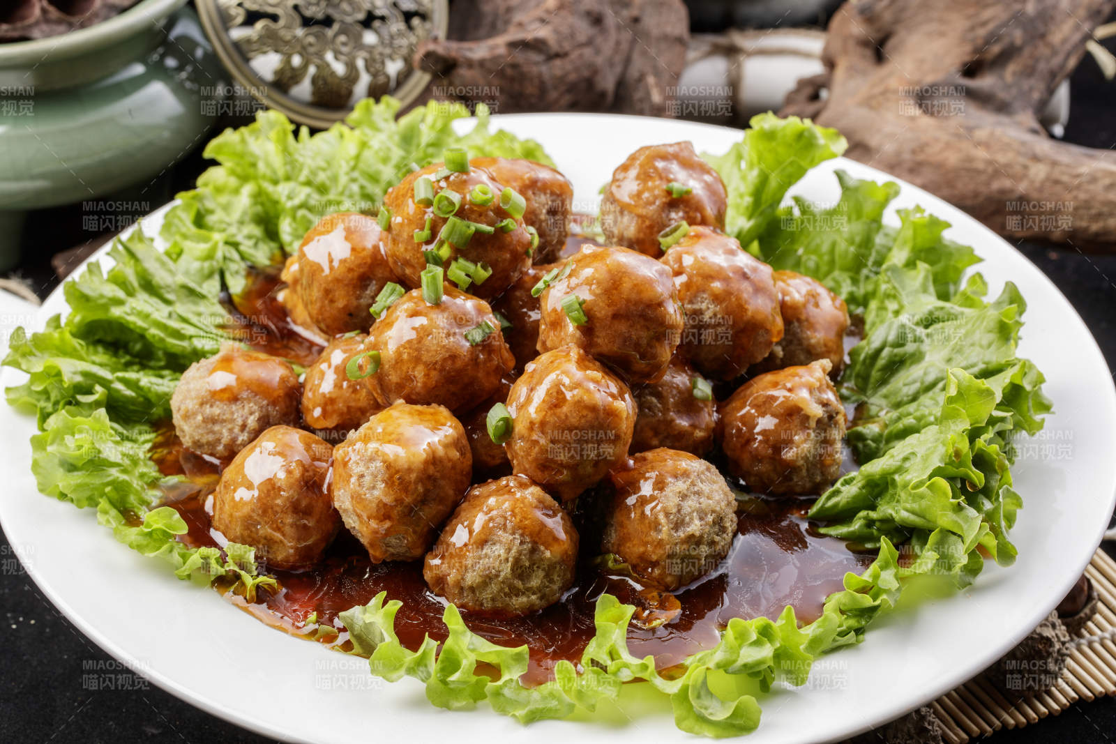 白色圆瓷盘装的红烧丸子摆放在樟木砧板上