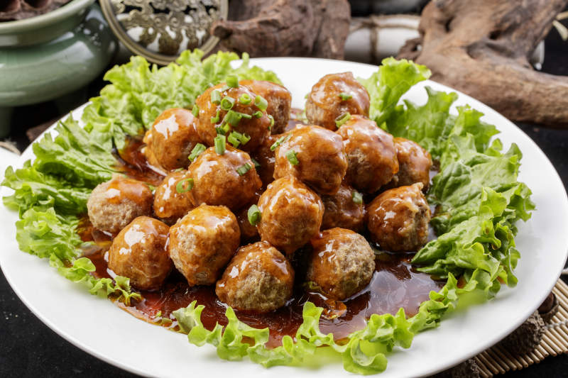 白色圆瓷盘装的红烧丸子摆放在樟木砧板上