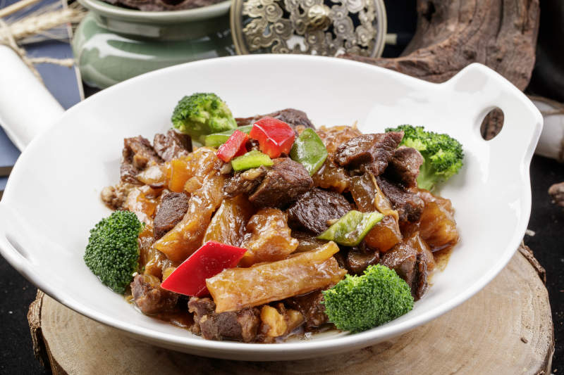 白色耳盘装的牛五花烧蹄筋摆放在樟木砧板上