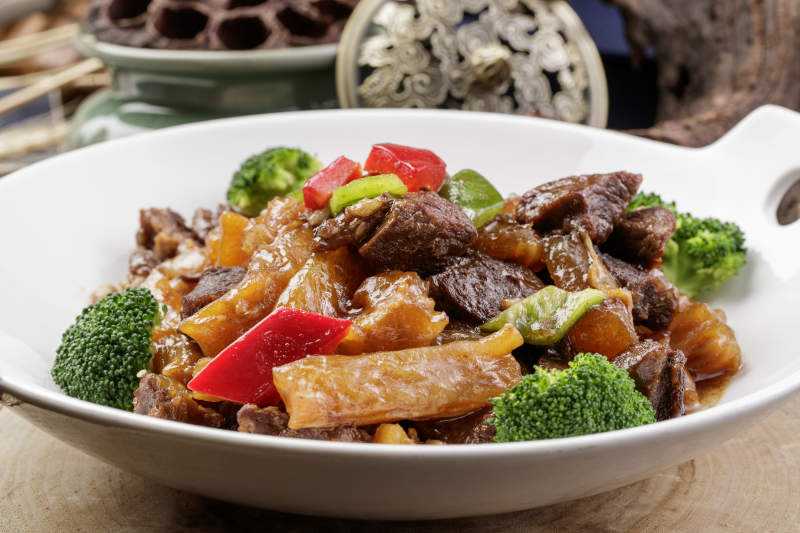 白色耳盘装的牛五花烧蹄筋摆放在樟木砧板上