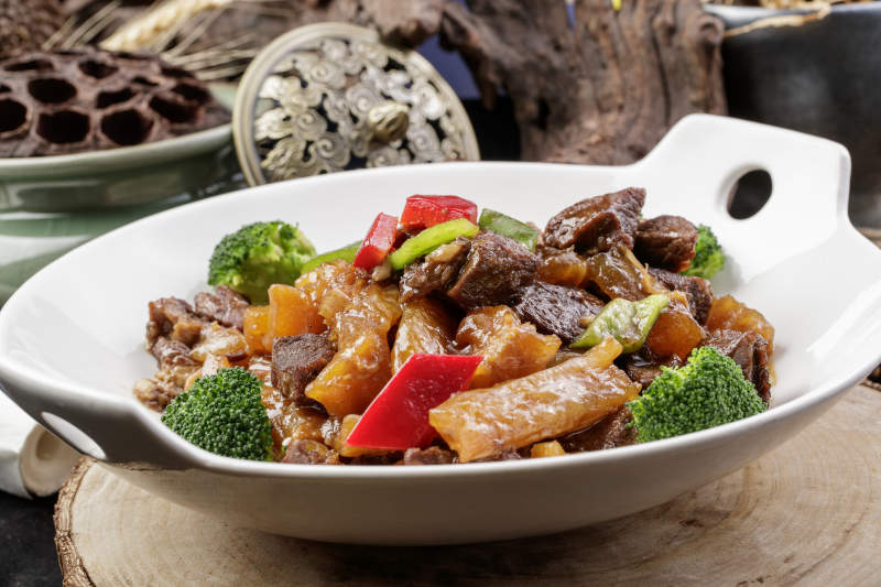 白色耳盘装的牛五花烧蹄筋摆放在樟木砧板上