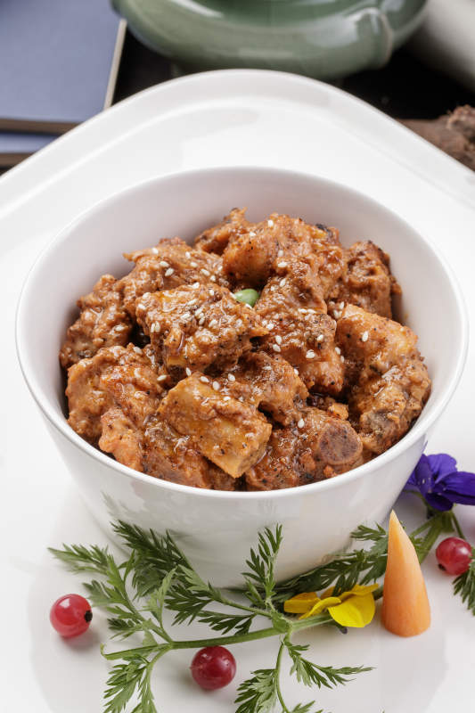 白色瓷碗装的黑胡椒猪小排摆放在黑色背景上