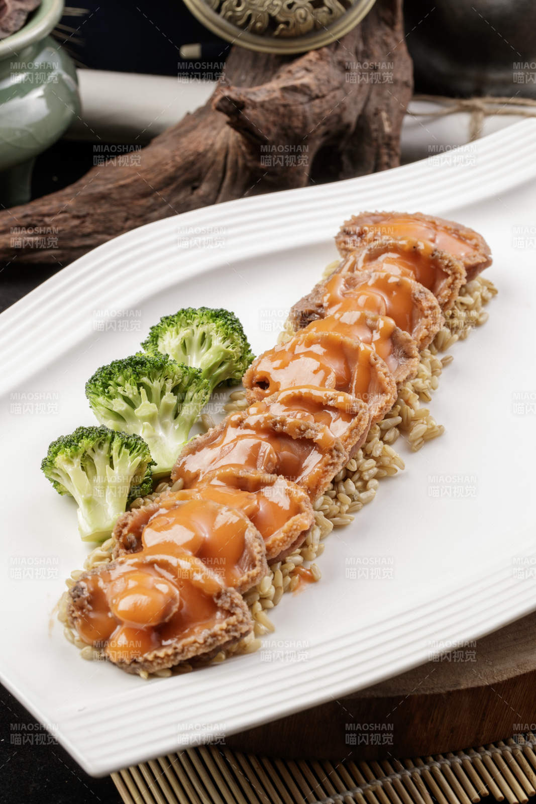 长方形瓷盘装的浓汁薏米鲜鲍鱼摆放在樟木砧板上