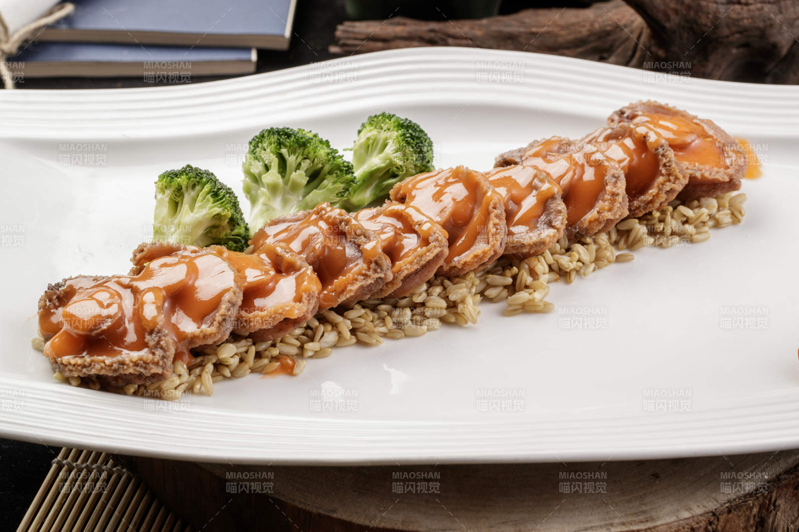 长方形瓷盘装的浓汁薏米鲜鲍鱼摆放在樟木砧板上