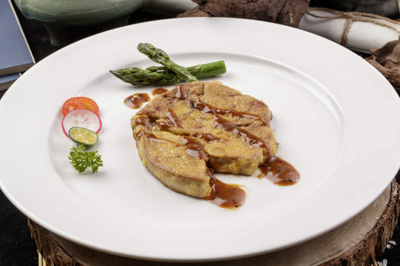 白色圆形瓷盘装的香煎法式鹅肝摆放在樟木砧板上