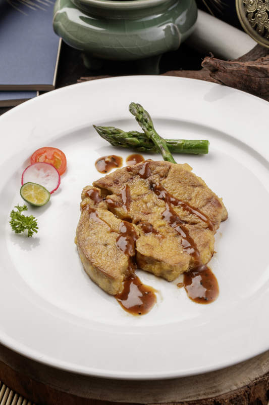 白色圆形瓷盘装的香煎法式鹅肝摆放在樟木砧板上