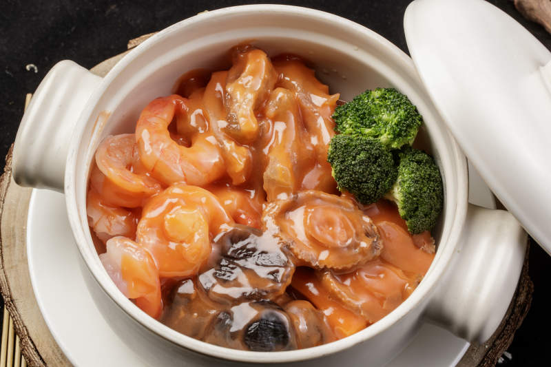 白色瓷砂锅装的浓汤海鲜煲摆放在寿司帘