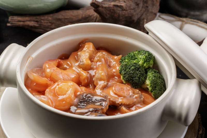 白色瓷砂锅装的浓汤海鲜煲摆放在寿司帘