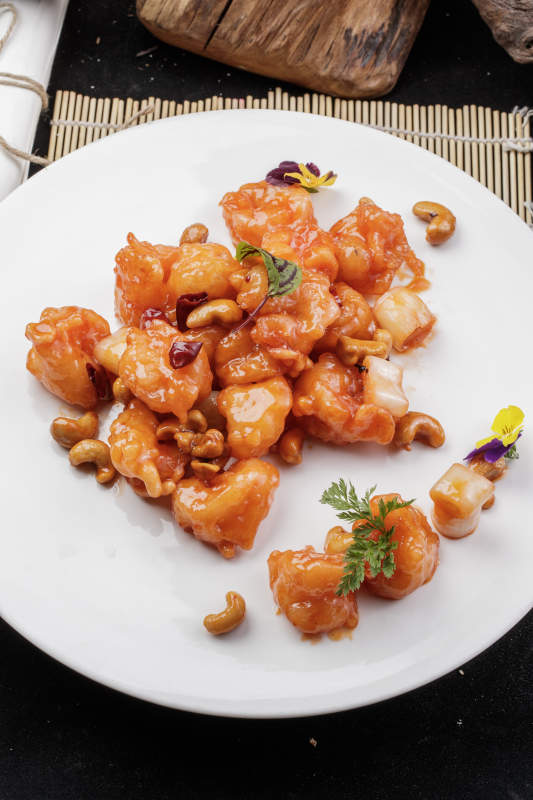 白色圆盘装的宫保大虾球摆放在寿司帘上