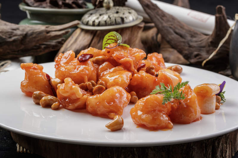 白色圆盘装的宫保大虾球摆放在寿司帘上