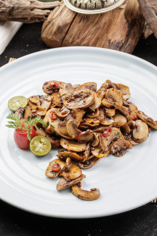 青瓷盘装的川味酱爆鲜口蘑摆放在寿司帘上