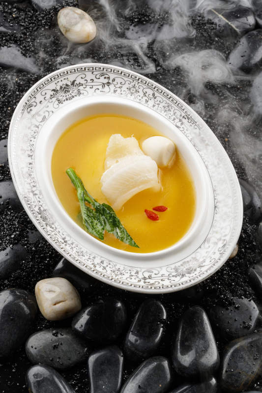 浓汤鱼唇摆放在干冰缭绕的鹅卵石上