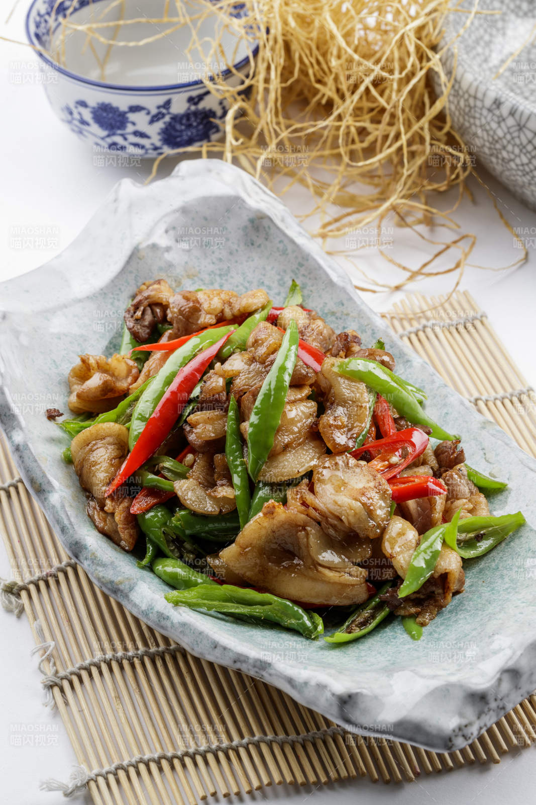 青瓷盘装的湘味小炒肉摆放在寿司帘上