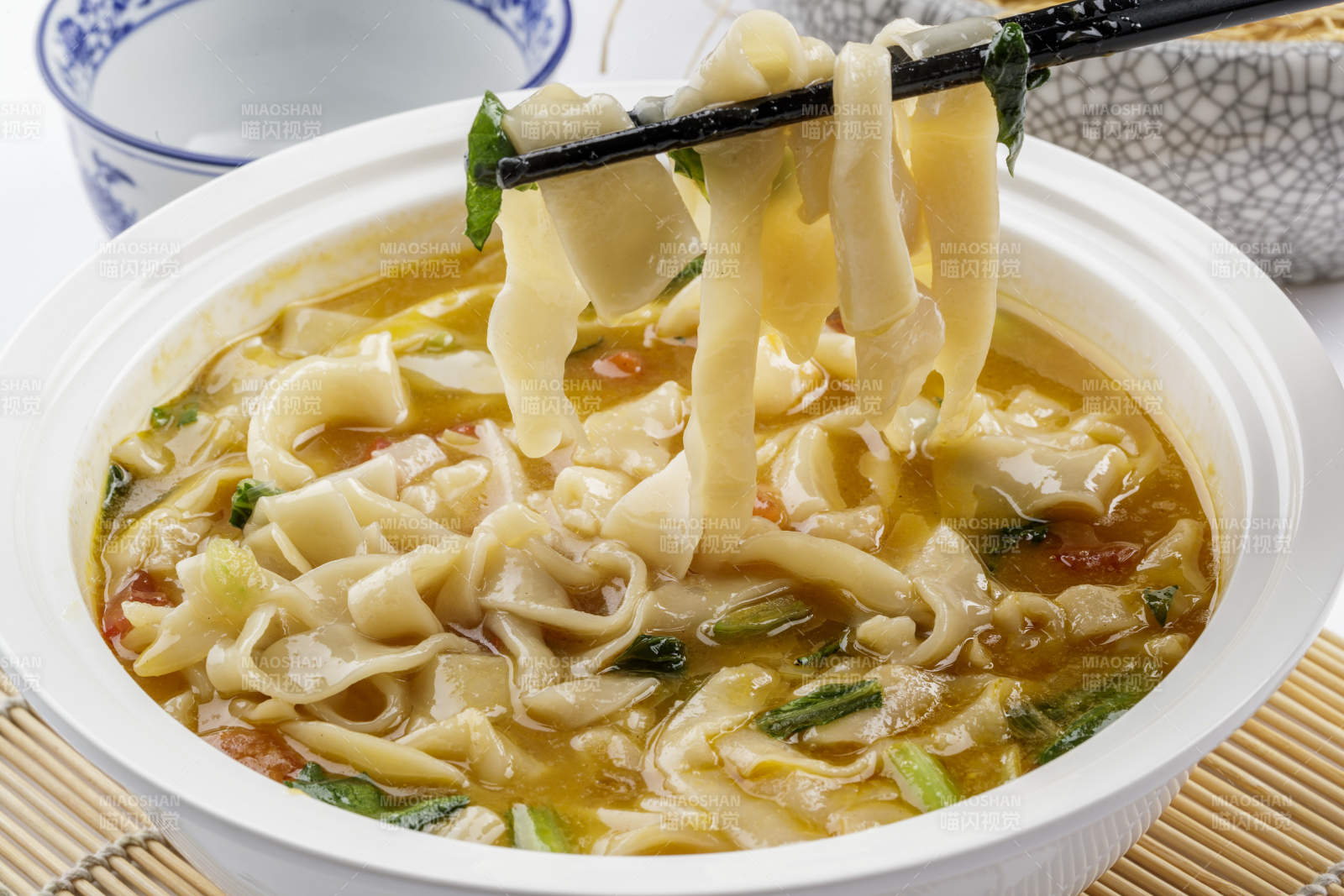 白色汤盆装的宽条打卤面摆放在寿司帘上