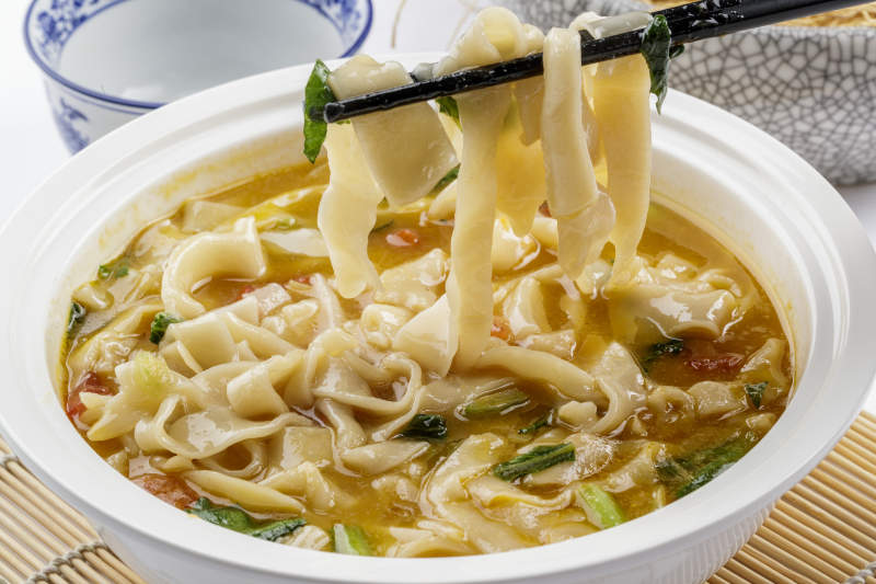 白色汤盆装的宽条打卤面摆放在寿司帘上