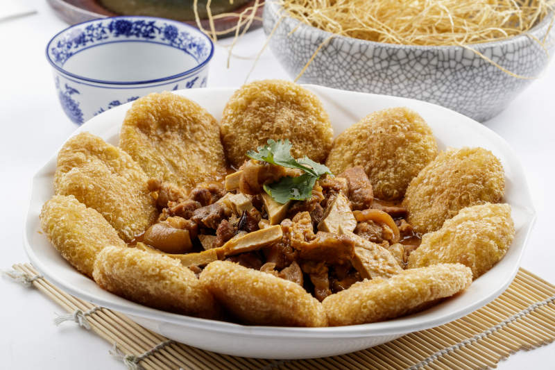 白色圆盘装的红扒肘子扒糕摆放在寿司帘上