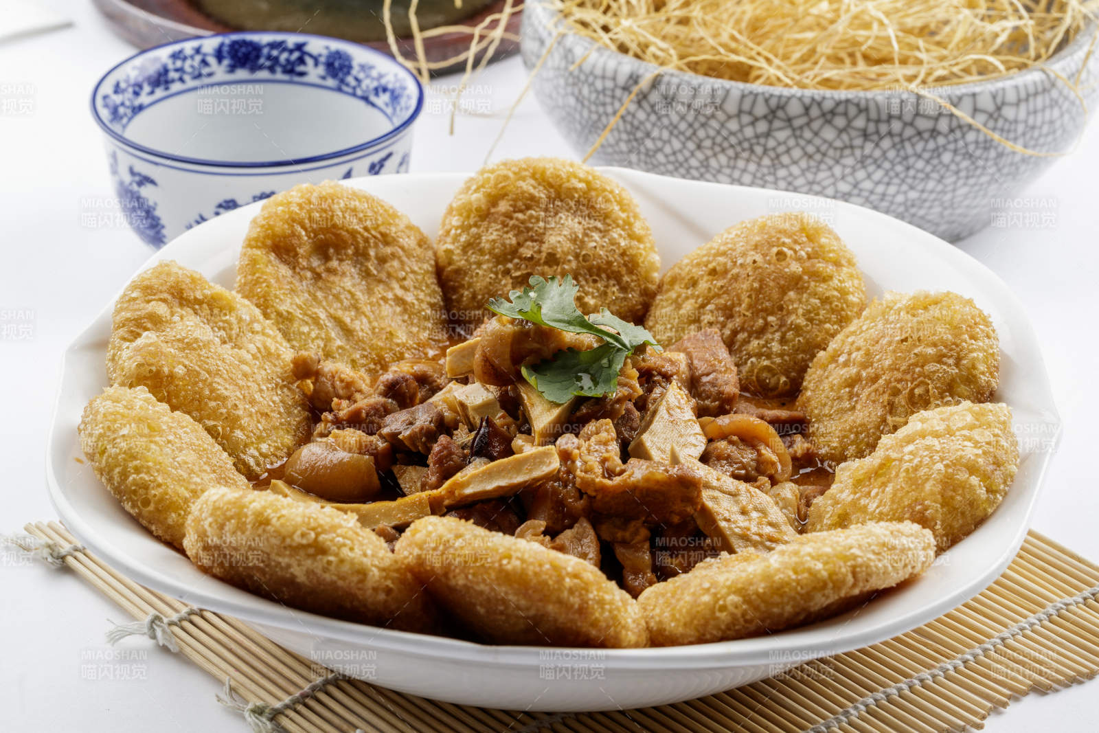 白色圆盘装的红扒肘子扒糕摆放在寿司帘上