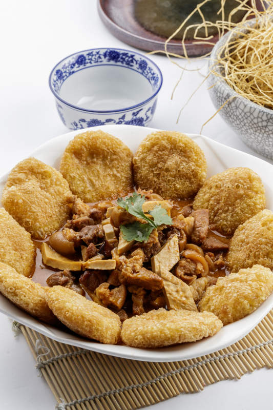 白色圆盘装的红扒肘子扒糕摆放在寿司帘上