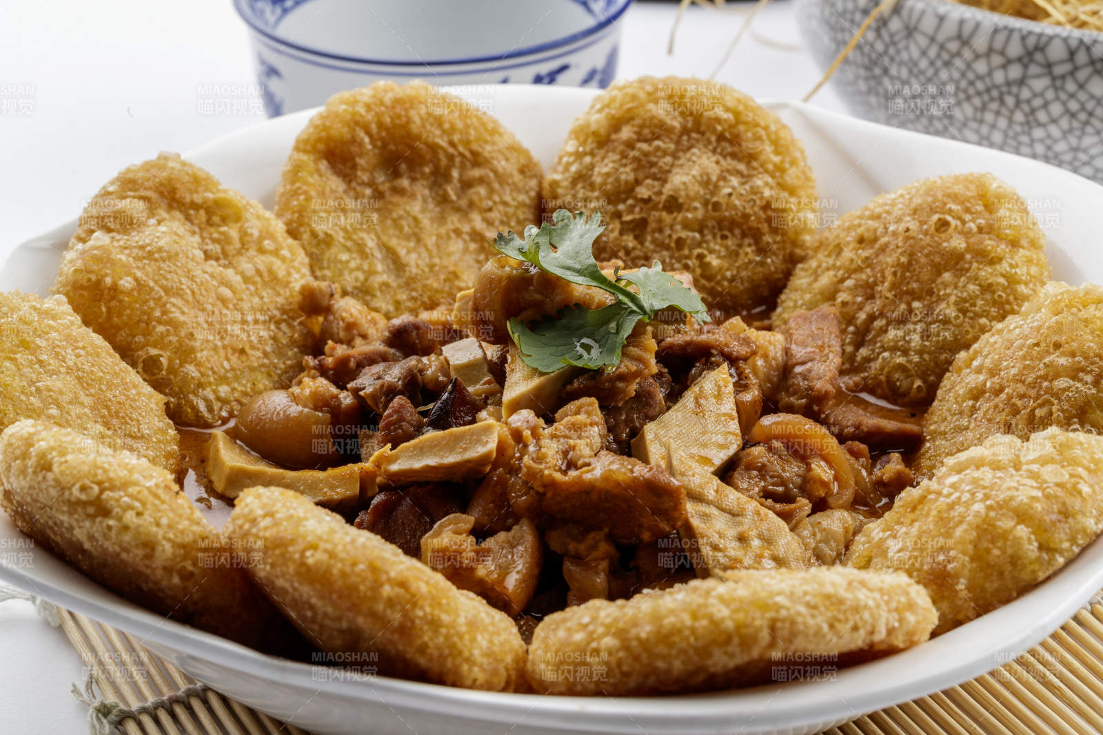 白色圆盘装的红扒肘子扒糕摆放在寿司帘上