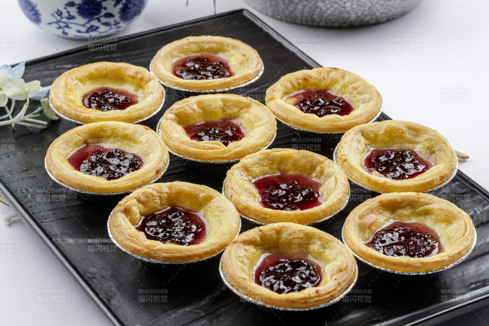 黑色盘子装的蓝莓蛋挞摆放在白色背景上