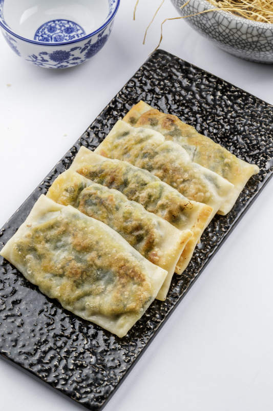 黑色磁盤裝的香酥韭菜盒子擺放在白色背景上