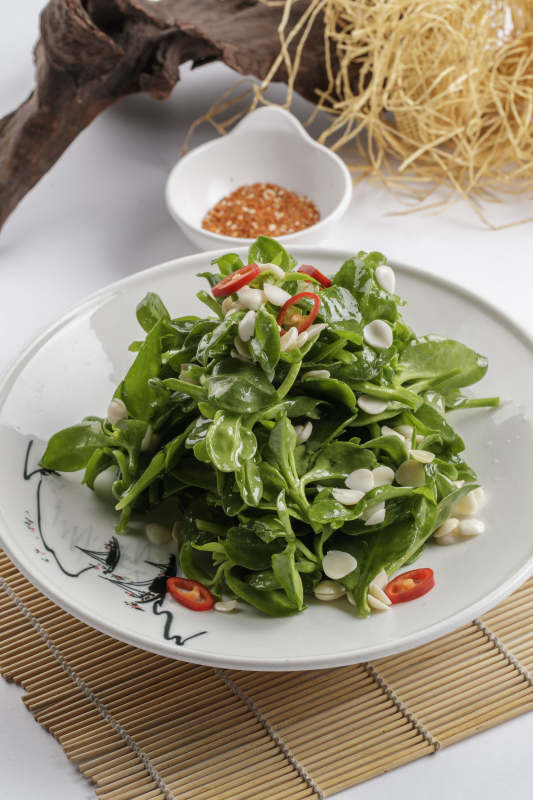 寿司帘上的圆瓷盘装的凉拌杏仁穿心莲