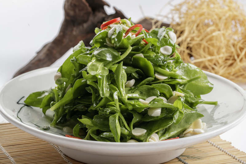 寿司帘上的圆瓷盘装的凉拌杏仁穿心莲