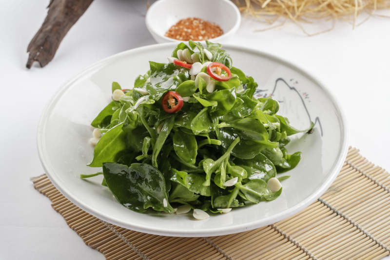 寿司帘上的圆瓷盘装的凉拌杏仁穿心莲