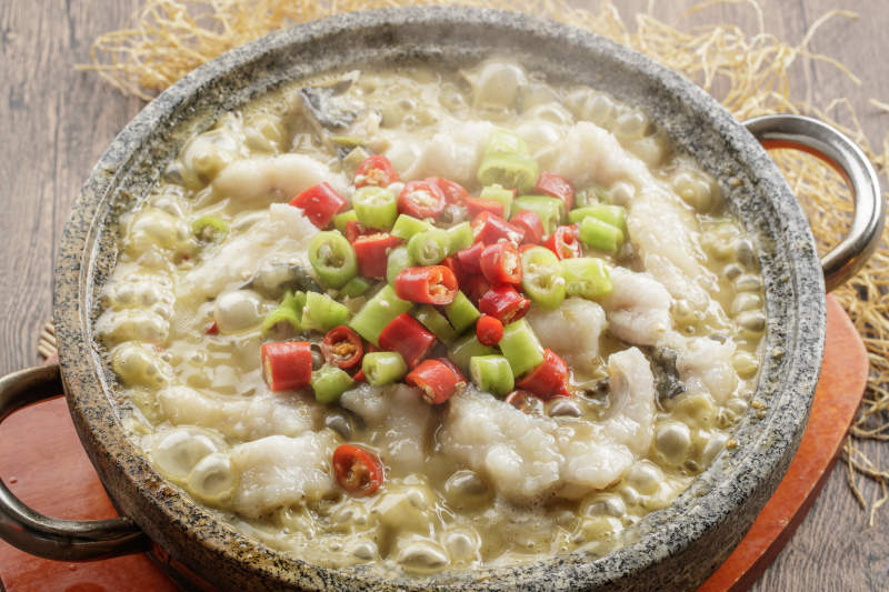 红木托盘上的石锅装的湘味沸腾鱼