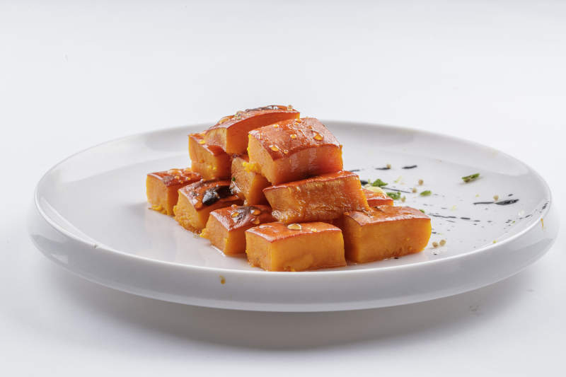 青瓷盘装的蜂蜜焗南瓜摆放在白色背景上