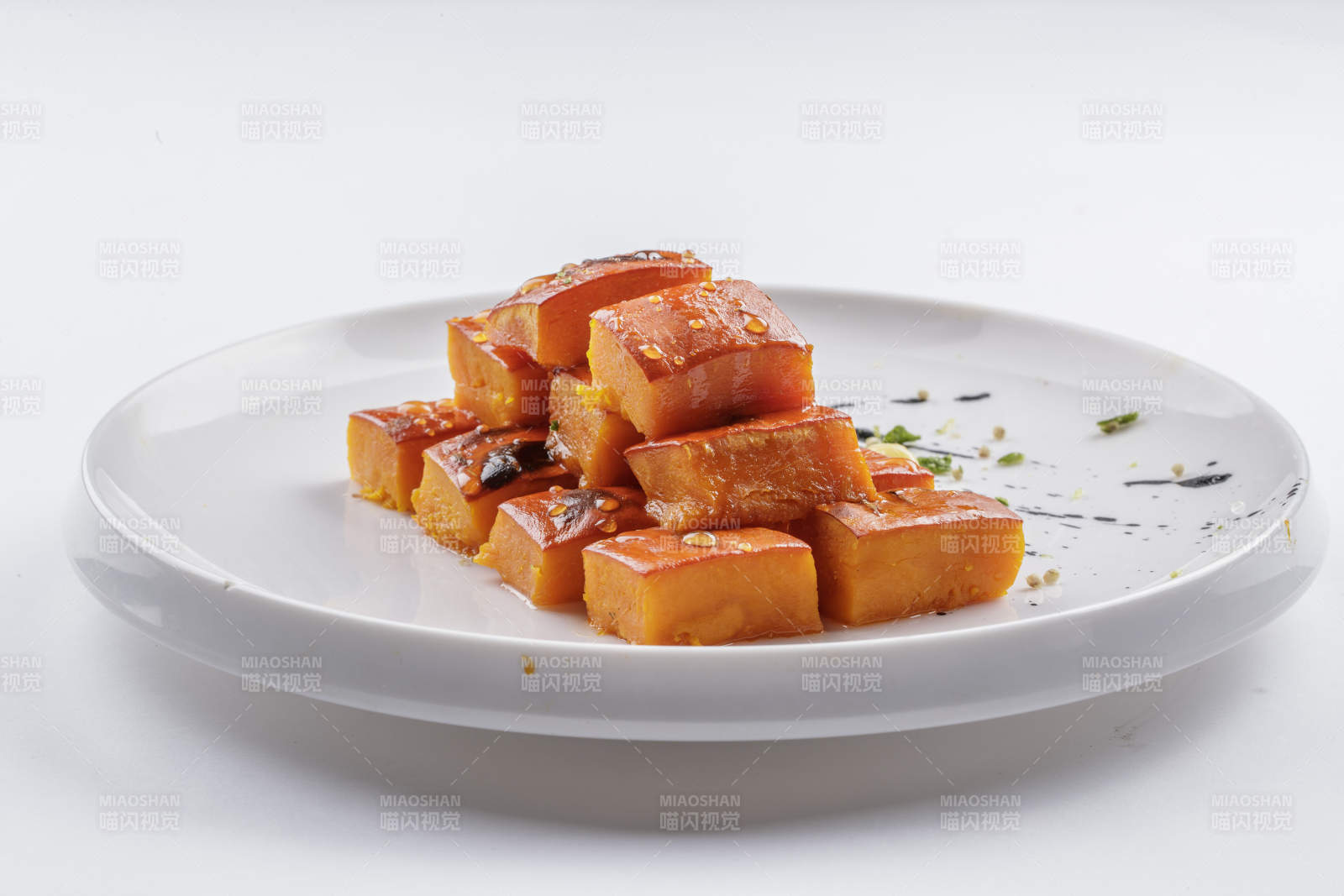 青瓷盘装的蜂蜜焗南瓜摆放在白色背景上