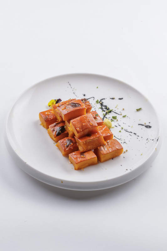 青瓷盘装的蜂蜜焗南瓜摆放在白色背景上