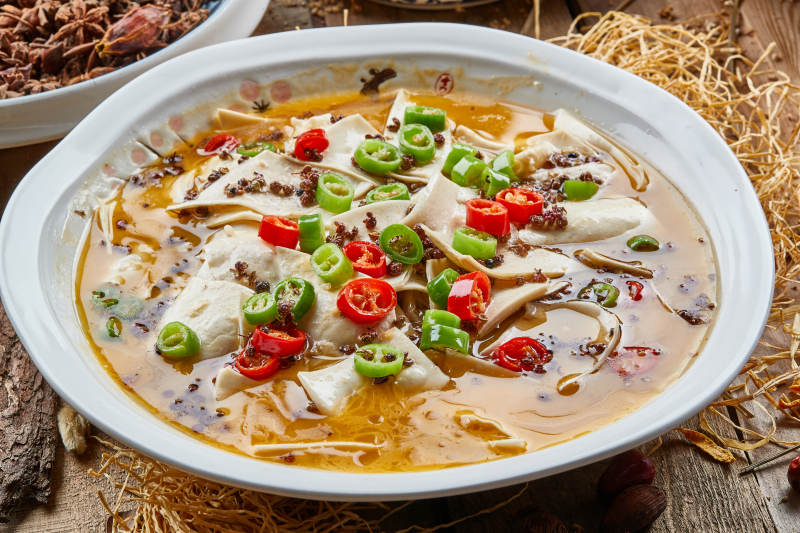 青瓷汤盆装的酸汤黄喉摆放在陈旧木板上