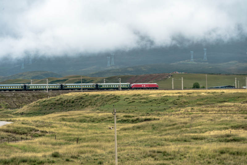 草原铁路上红色列车穿过云雾驶过高原山峦间