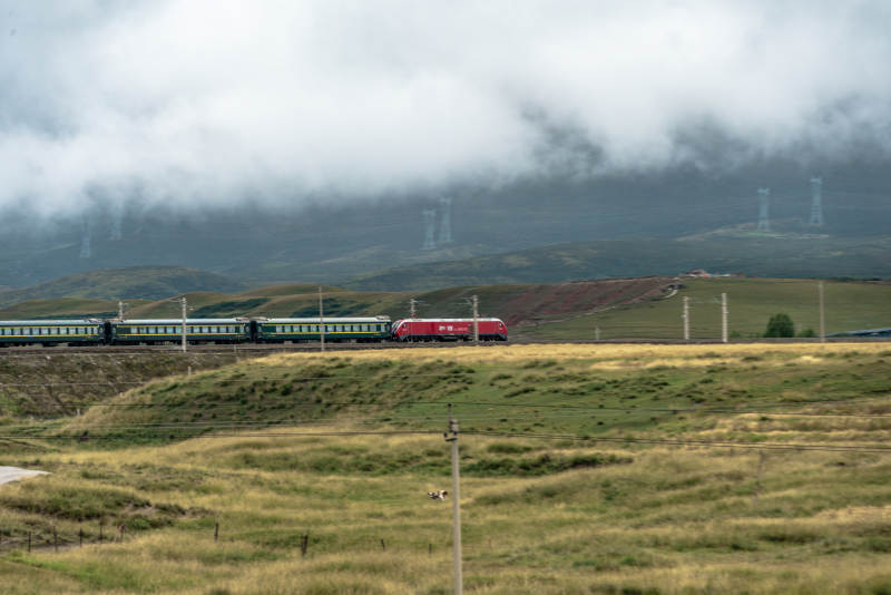 高山草原上和谐号机车牵引绿皮火车穿云行驶