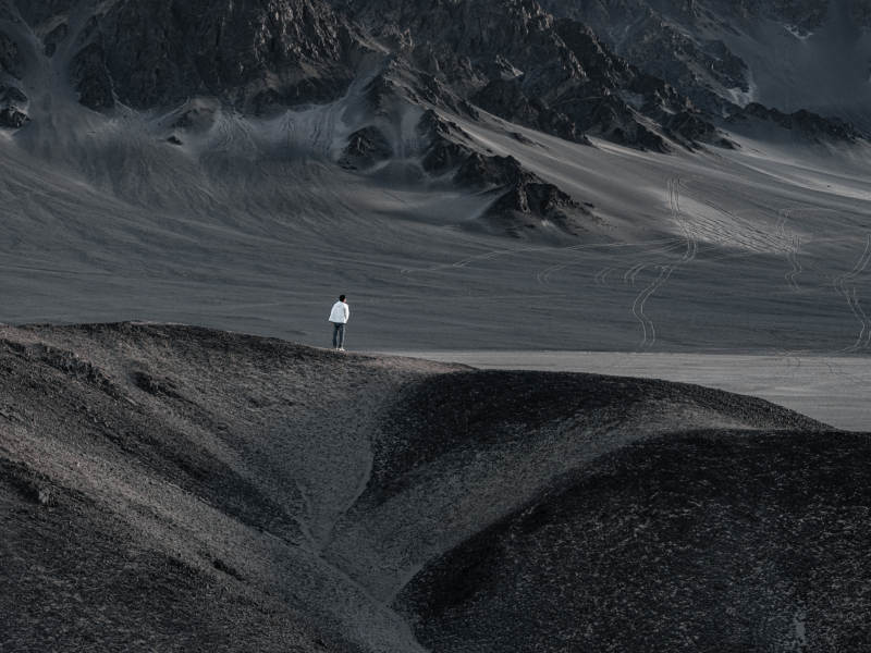 孤独旅人站立在荒凉山地眺望探索远方沙漠