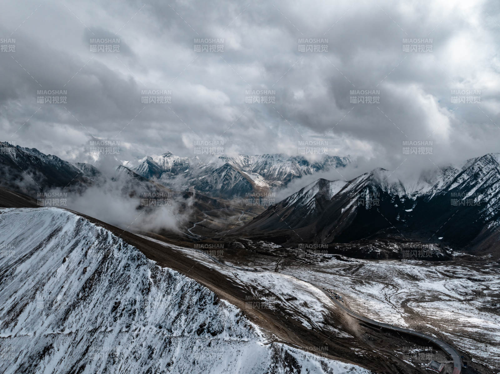 雪山云雾缭绕下蜿蜒道路点缀的高山壮丽景观