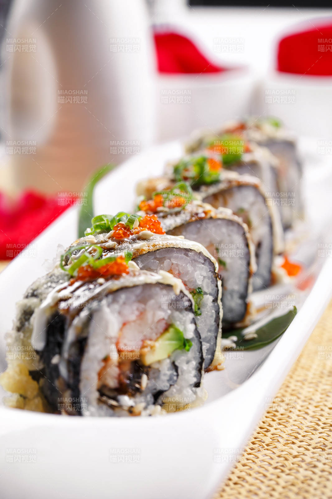 椭圆长瓷盘装的鹅肝手卷寿司摆放在草垫上
