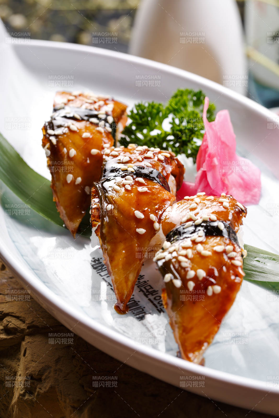 鹅颈白瓷盘装的烤鳗鱼手握寿司摆放在石头上