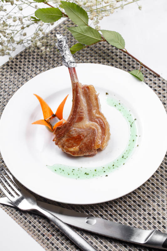 圆形白瓷盘装的波尔多法式铁板羊排摆放在餐垫上