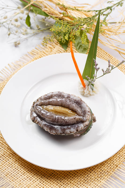 圓形瓷盤裝的生鮮活鮑魚擺放在草墊上