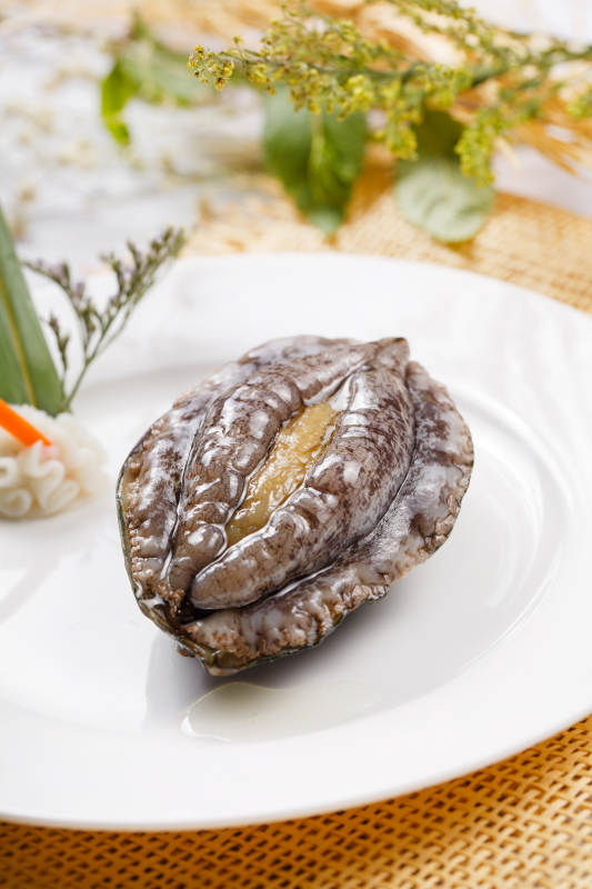 圓形瓷盤裝的生鮮活鮑魚擺放在草墊上