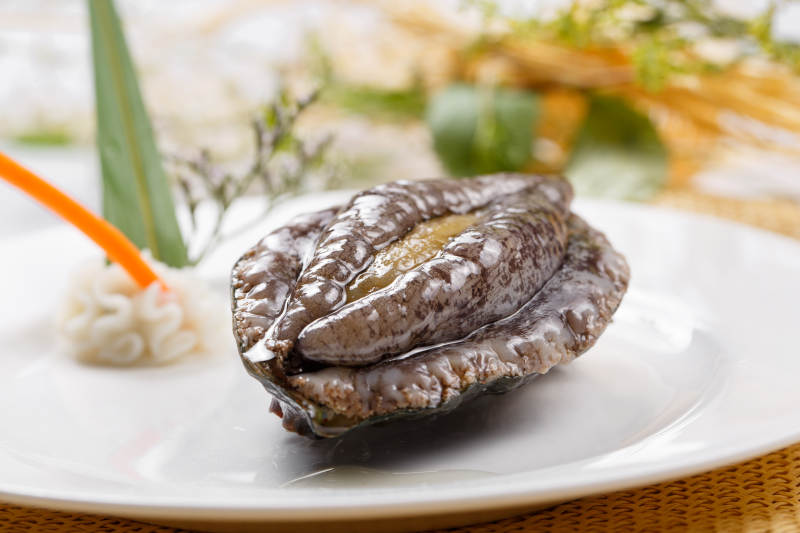 圓形瓷盤裝的生鮮活鮑魚擺放在草墊上