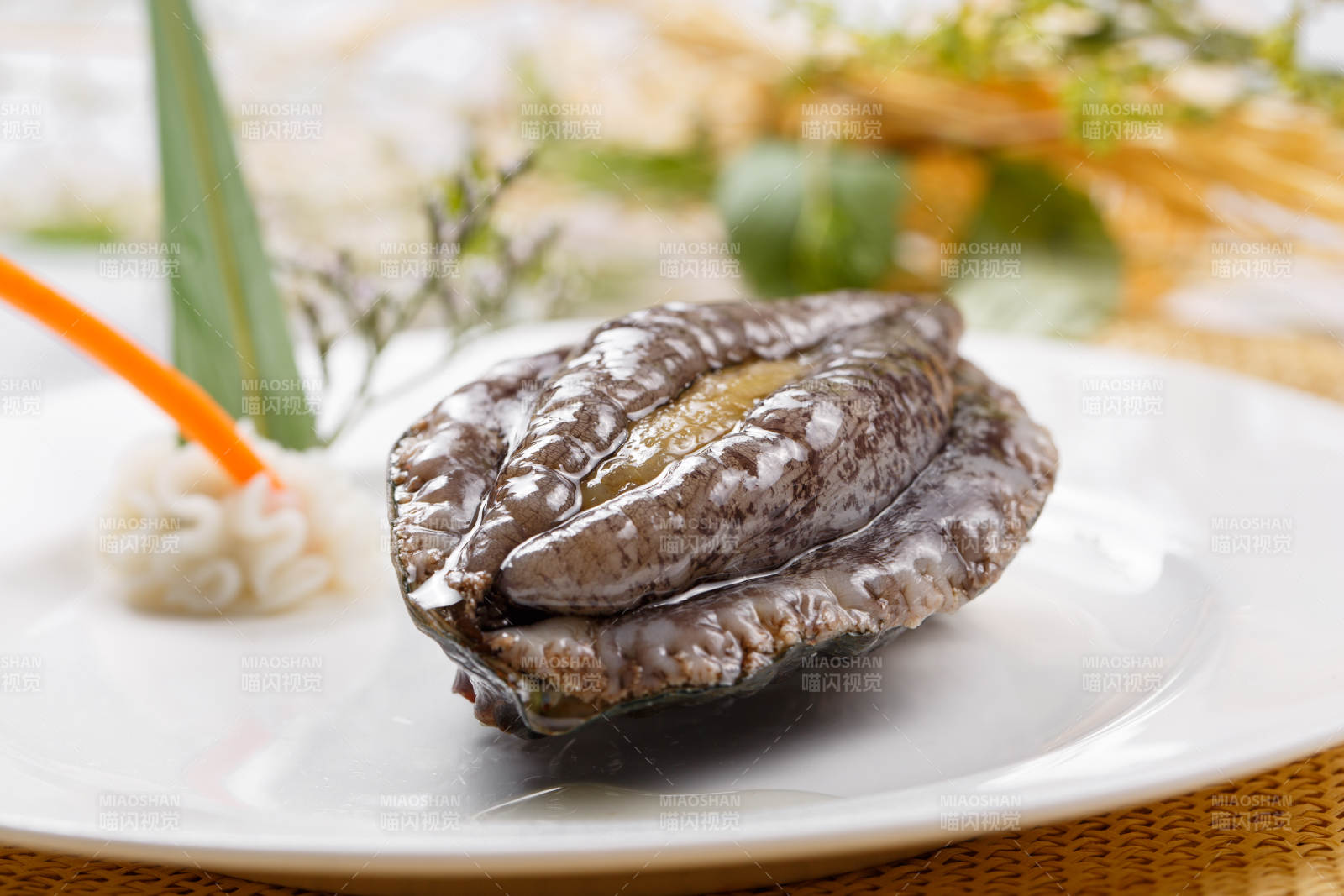 圓形瓷盤裝的生鮮活鮑魚擺放在草墊上