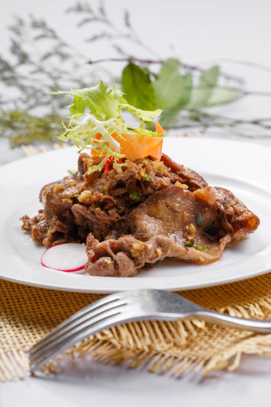 圆形白瓷盘装的铁板蒜香牛舌摆放在草垫上