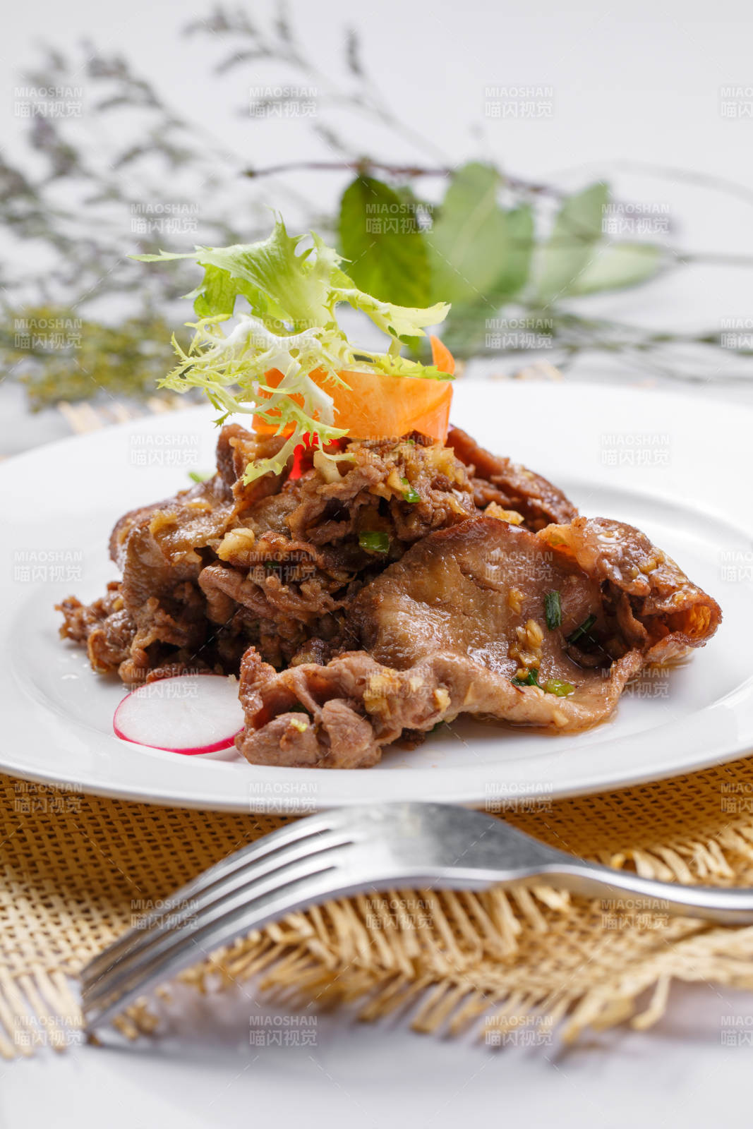 圆形白瓷盘装的铁板蒜香牛舌摆放在草垫上