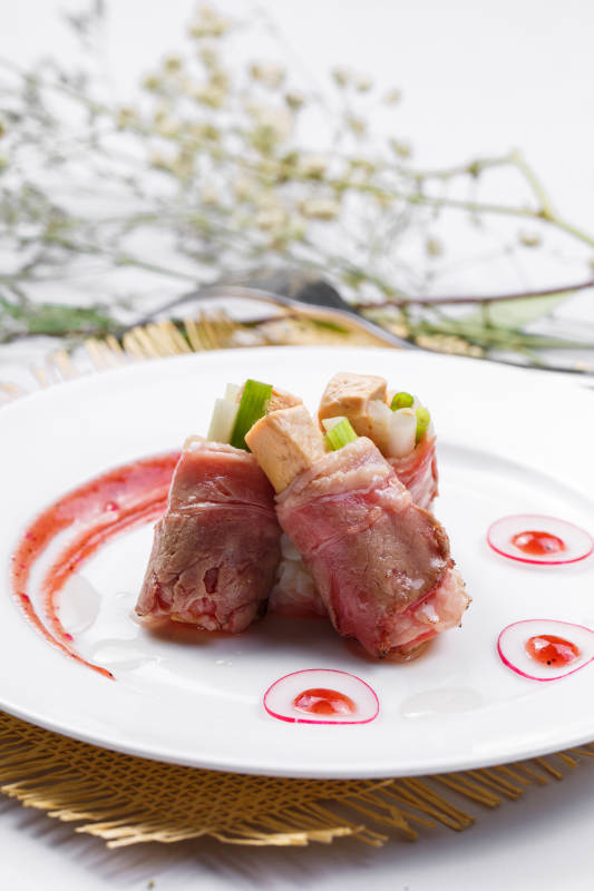 白色圆盘装的法式鹅肝牛肉卷摆放在草垫上