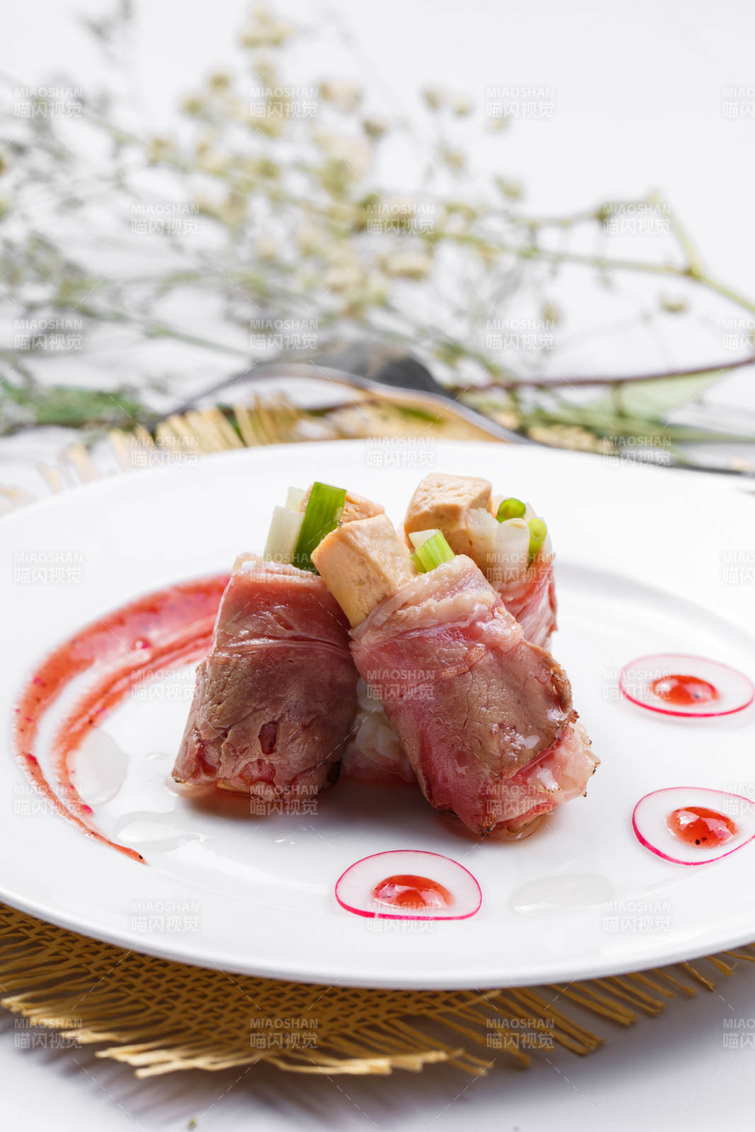 白色圆盘装的法式鹅肝牛肉卷摆放在草垫上