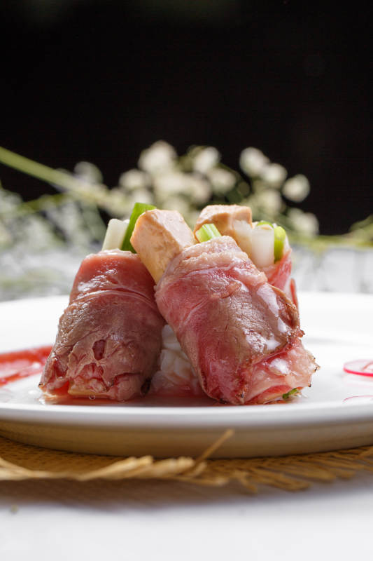 白色圆盘装的法式鹅肝牛肉卷摆放在草垫上