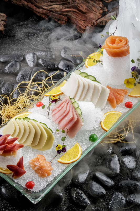 刺身拼摆放在干冰缭绕的黑色鹅卵石上